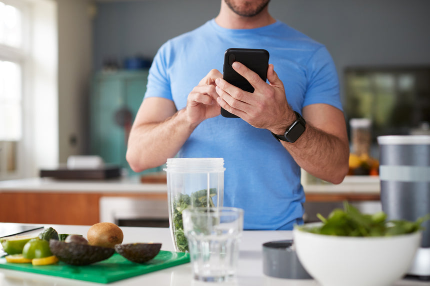 Close Up Of Man Using Fitness Tracker To Count Calories For Post Workout Juice Drink He Is Making