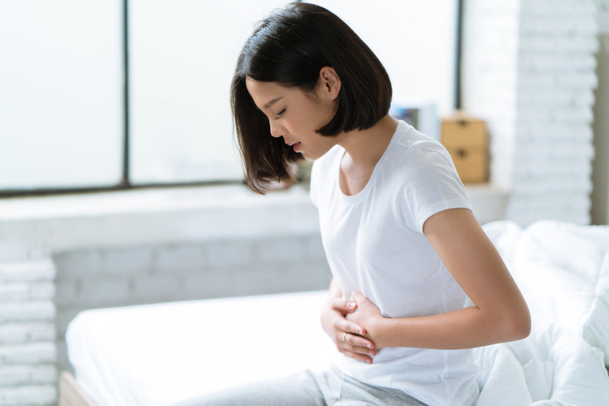 Woman with a stomach ache places hands on stomach in bed